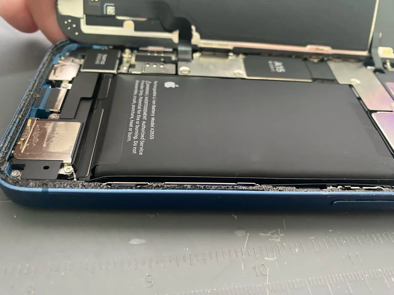 Bateria de iPhone estufada vista de lado, com o aparelho aberto na bancada da assistência técnica