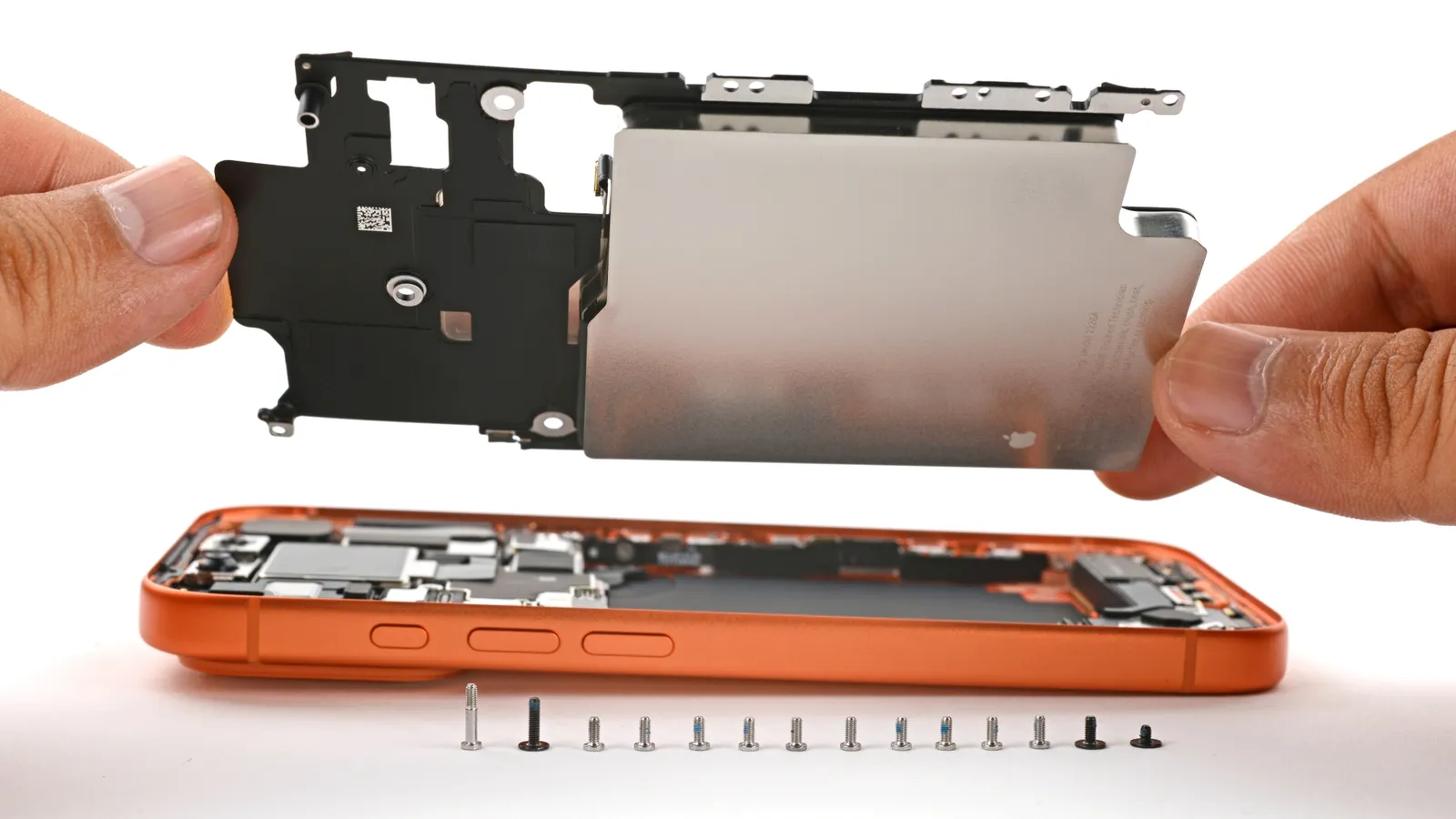 Bateria e suporte internos sendo retirados de um iPhone aberto, ao lado dos parafusos
